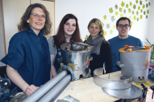 An diesem Holztresen in Sebastian Erdmanns (rechts) Wohnung entstanden das Pappmodell und der erste richtige Herd. Christiane Richter und Lia Weiler (von links) präsentieren hier die Modelle. Auf dem Foto fehlt der Vierte im Bunde, Markus Espeter. Mit dabei ist Annika Wallbach, die als Mitarbeiterin von UniKasselTransfer mit Hilfe der Crowdfunding-Seite Unterstützer für das Projekt GloW einwirbt. Foto: Mario Zgoll An diesem Holztresen in Sebastian Erdmanns (rechts) Wohnung entstanden das Pappmodell und der erste richtige Herd. Christiane Richter und Lia Weiler (von links) präsentieren hier die Modelle. Auf dem Foto fehlt der Vierte im Bunde, Markus Espeter. Mit dabei ist Annika Wallbach, die als Mitarbeiterin von UniKasselTransfer mit Hilfe der Crowdfunding-Seite Unterstützer für das Projekt GloW einwirbt. Foto: Mario Zgoll