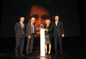 Bernd Leifeld (Vorstandsvorsitzende des Fördervereins „Das Glas der Vernunft“, Oberbürgermeister Bertram Hilgen, Barbara Ettinger-Brinckmann (stellv. Vorsitzende des Fördervereins) und Dieter Mehlich (ebenfalls stellv. Vorsitzender des Fördervereins) – im Hintergrund: Edward Snowden war über eine „Skype“-Verbindung live aus Moskau zugeschaltet. Foto: Harry Soremski